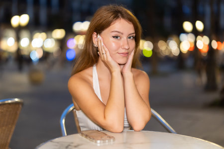 Woman sits at a table in a cafe overlooking the evening city of Barcelonaの写真素材