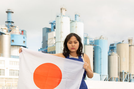 Sad young woman with flag of Japan against background of factoryの写真素材
