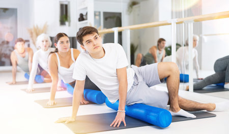 Active vigorous man performs exercises with a pilates roller while on a mat in the hall of a modern...