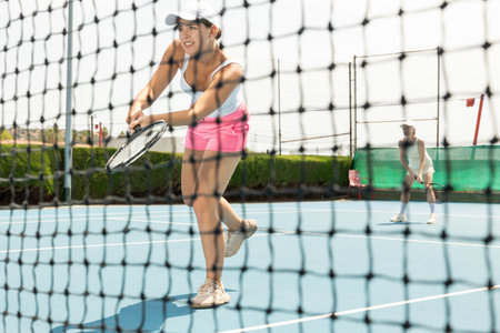 Sporty girl tennis player playing tennis. View through tennis netの写真素材