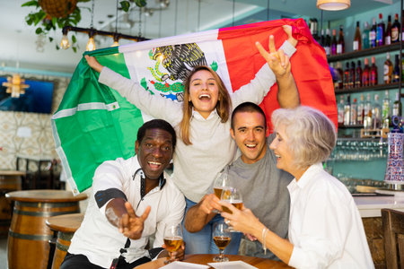 Excited multiracial soccer fans with flag of Mexico celebrating victory with pint of beer in the pubの写真素材