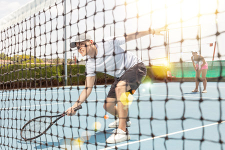 Portrait of young man tennis player during doubles couple match at court. View through tennis netの写真素材