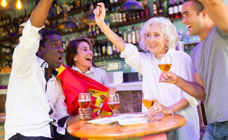 Excited multicultural football fans celebrate goal score of their team with hands up at pubの写真素材
