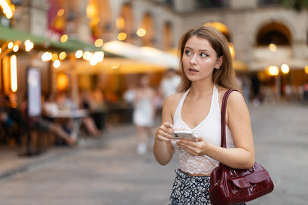 Woman in summer dress walks along the evening street of Barcelona against the backdrop of cafes and restaurants with romantic lightingの写真素材