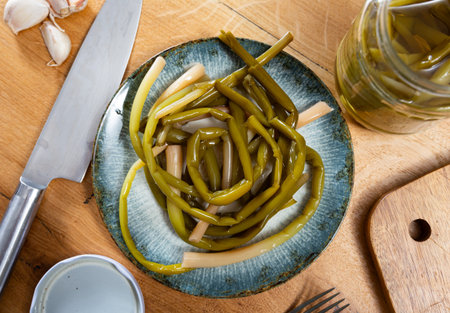 Pickled ramson is laid out on plate, next to it is cutting board, garlic cloves, knife and cutting boardの写真素材