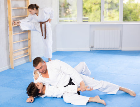 Judo or jiu-jitsu classes - two men practicing grabbing and throwing on sports mats under the guidance of trainerの写真素材