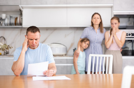 Disgruntled father carefully reads documents. The whole family stands in fear in backgroundの写真素材