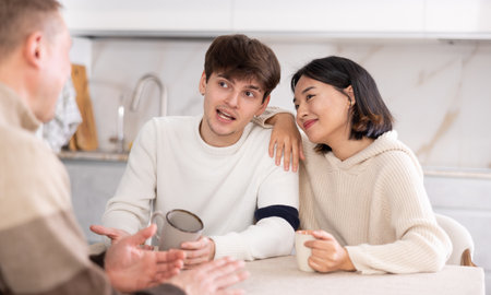Happy family chatting and drinking tea together in home kitchenの写真素材