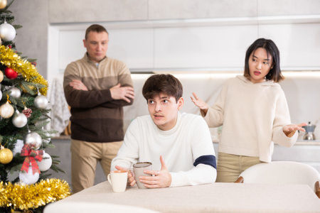 Quarrel during Christmas celebration - father and sister scolding young guy in home kitchenの写真素材