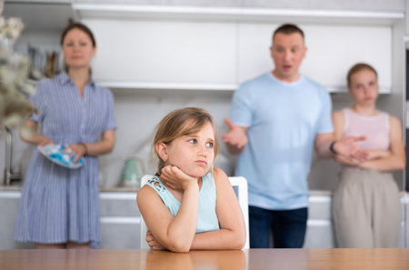 At home kitchen parents scold sitting child for bad behavior, mother clean dish in backgroundの写真素材