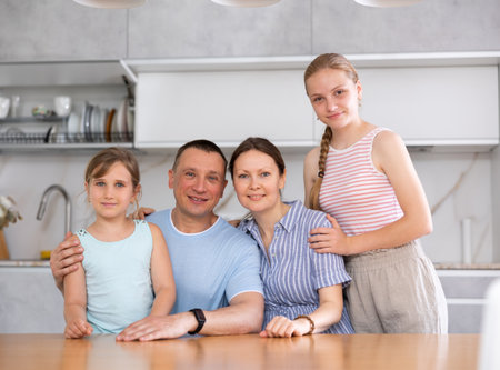 Happy family of four people is posing at kitchen tableの写真素材