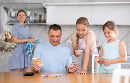 Father gives pocket money to children and wife in kitchenの写真素材