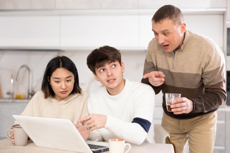 Adult man and young couple using laptop in kitchenの写真素材