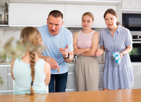 Displeased mother and father reprimanding preteen girl in home kitchenの写真素材