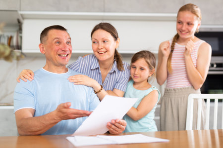 Happy man with wife and teenage daughters reading notification at homeの写真素材