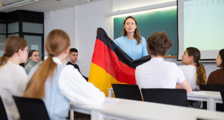 High school teacher holds the flag of Germany in her hands and talks about this country in geography lessonの写真素材