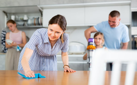 Mom is dusting the table. Father with children vacuuming room