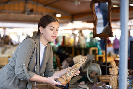 Satisfied young woman choosing interesting antique things at traditional flea marketの写真素材