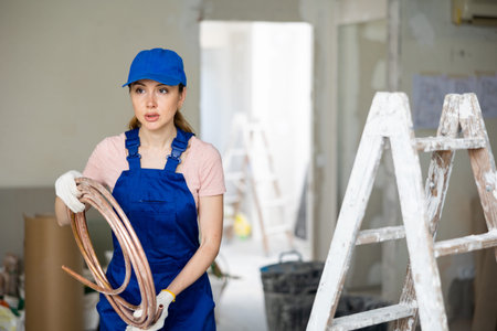 Portrait of female builder in blue overalls with floor heating tubes in hands