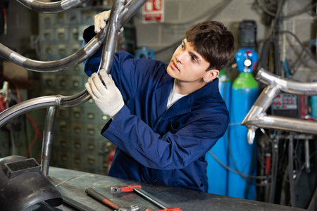 Portrait of male welder standing with welding machine and safety helmet in metal machining workshopの写真素材