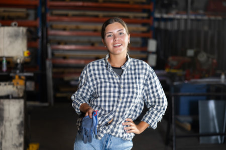 Smiling young female worker standing in metal workshopの写真素材