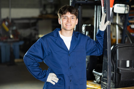 Young guy posing by forklift in workshop