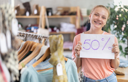 Teenage girl holding discount sign in clothing storeの写真素材