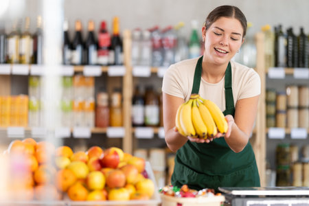 Young woman seller offering bananas in grocery storeの写真素材