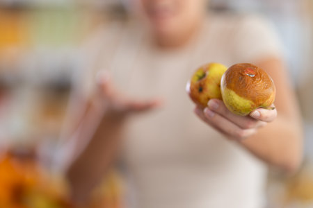In store, frustrated girl holds rotten fruits in hands, close-upの写真素材