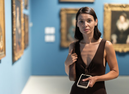 Woman with phone in hands in museum hall, view painting exhibitionの写真素材
