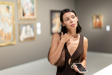 Woman with phone in hands in museum hall, view painting exhibitionの写真素材