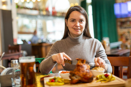 Smiling woman enjoying baked pork knuckle in restaurantの写真素材