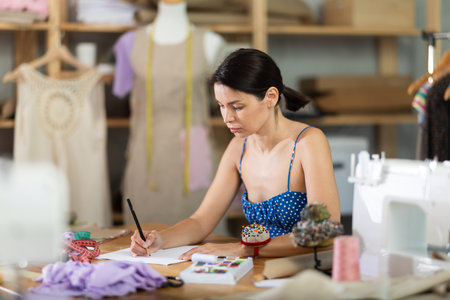 Young woman seamstress draws sketch on paperの写真素材