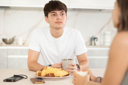 Happy young couple sitting at the kitchen-table and having conversation while drinking teaの写真素材