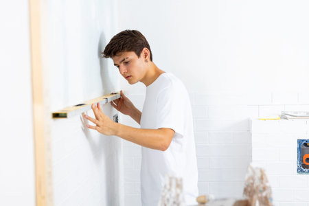 Guy inspecting quality of tiles laid on walls with level meterの写真素材