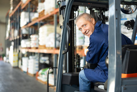Elderly man worker works on loader in warehouseの写真素材