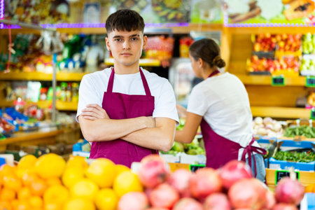Portrait of positive young salesman in the vegetable section of grocery storeの写真素材