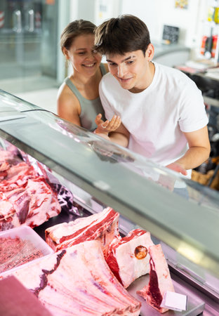 Young man and woman purchasers buying meat in butcher shopの写真素材