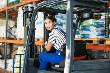 Girl works on fork lift loader in construction rack area warehouse store repair materials.の写真素材