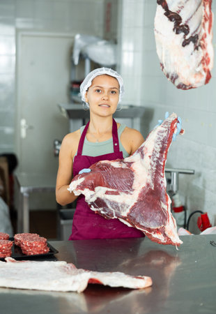 Girl in butcher shop cuts meat carcass into small pieces of meat for retail sale in small storeの写真素材