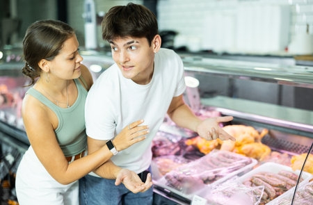Young man and woman purchasers buying sausages in butcher shopの写真素材