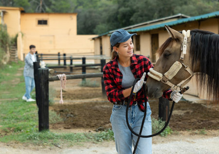 Portrait of female owner of horse farm shows her farm against backdrop of corral for walking horses