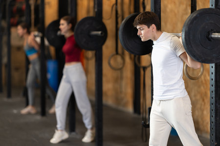 Slender guy trains muscles of arms and back using barbell and differentiated weighting in gymの写真素材