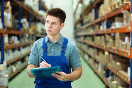 Man storekeeper keeps track of goods on the shelves of construction warehouse or storeの写真素材