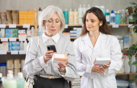 Senior woman in pharmacy scans QR code on omega 3 supplement, woman pharmacist in backgroundの写真素材