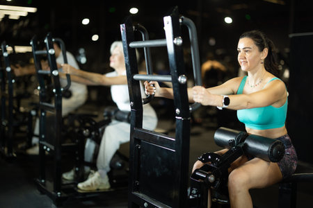 Woman performing resistance sit-to-stand exercise on machine at gymの写真素材