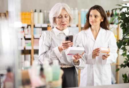 Senior woman in pharmacy scans QR code on omega 3 supplement, woman pharmacist in backgroundの写真素材