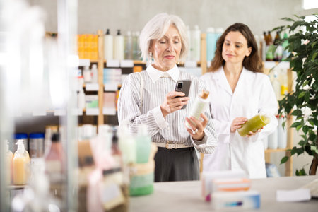 Mature woman scanning shampoo with pharmacist backgroundの写真素材