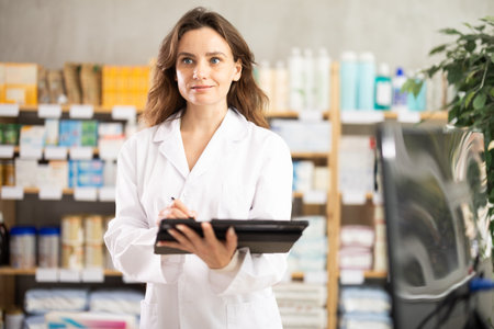 Female seller makes notes on electronic tablet - keeps track of receipt and expenditure of pharmacyの写真素材