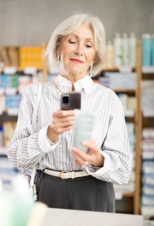 Mature woman in summer clothes scans code on package of cream to check expiration dateの写真素材